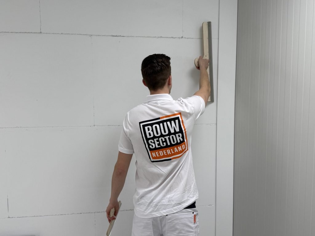 Achteraanzicht van een stukadoor van Bouwsector Nederland die met twee spanen een wand afwerkt
