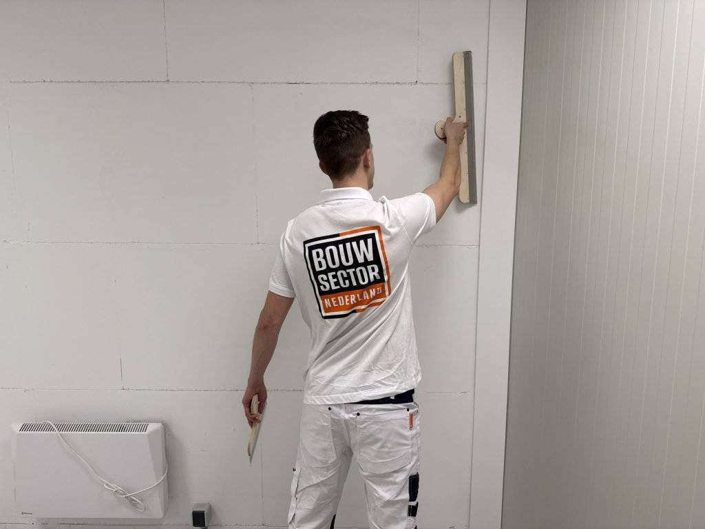 Stukadoor met het logo van Bouwsector Nederland op zijn rug zet de spaan hoog op de muur