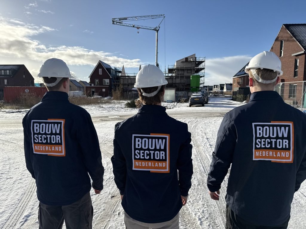 Drie vakmensen van Bouwsector Nederland met witte helm kijken uit over een bouwplaats in de sneeuw