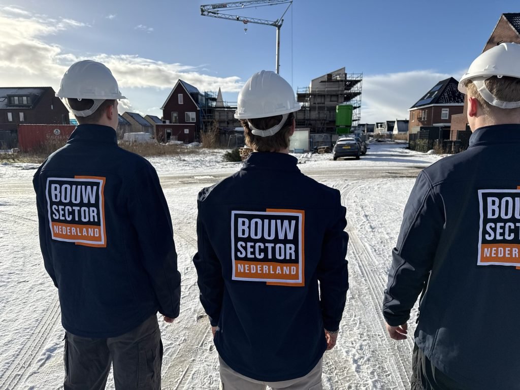 Vakmensen van Bouwsector Nederland in winterjassen tussen nieuwe woningen en een bouwkraan