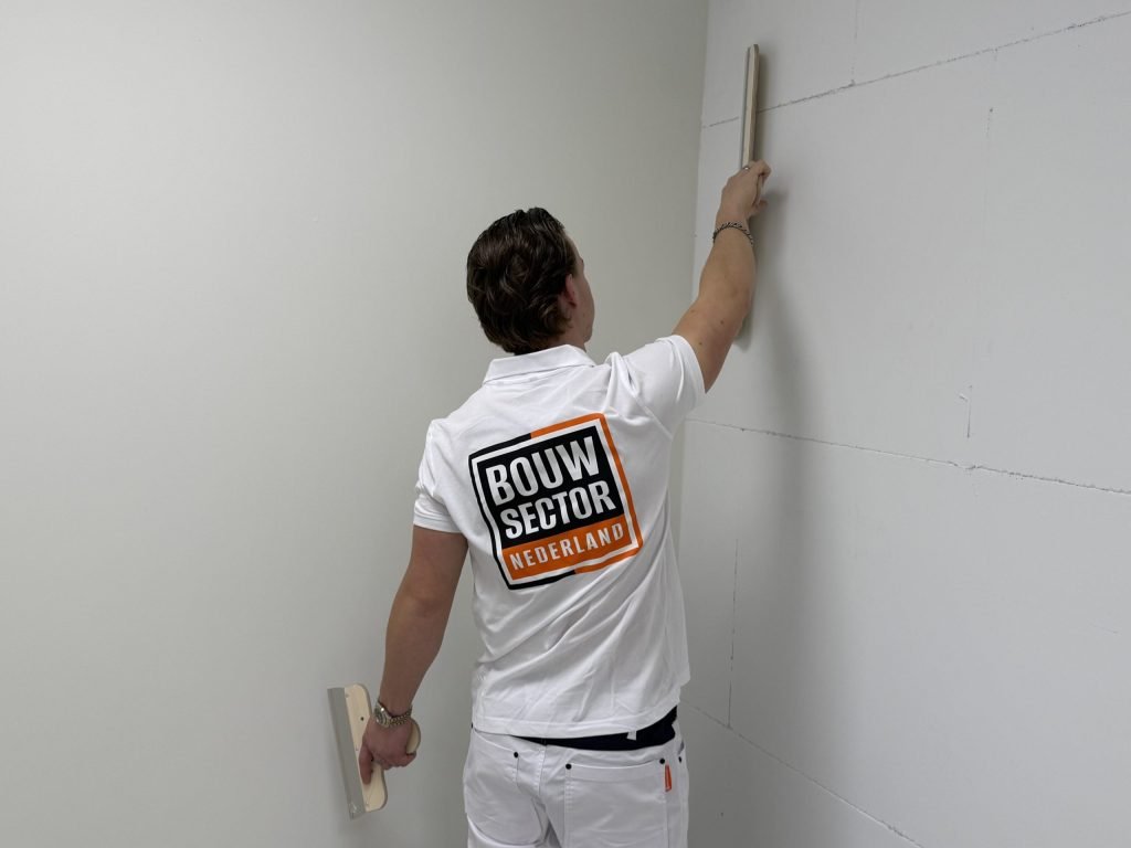 Stukadoor van Bouwsector Nederland strijkt met een lange spaan een wand in de hoek van de kamer vlak