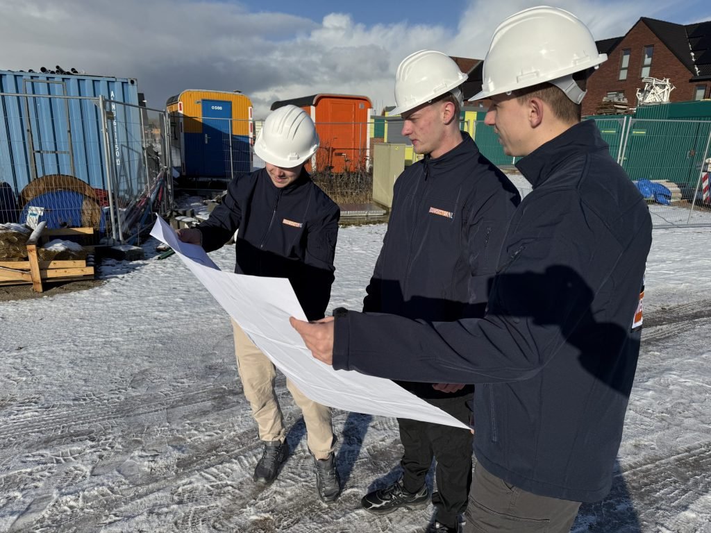 Drie medewerkers van Bouwsector Nederland met witte helm buigen zich over een bouwtekening op een nieuwbouwterrein